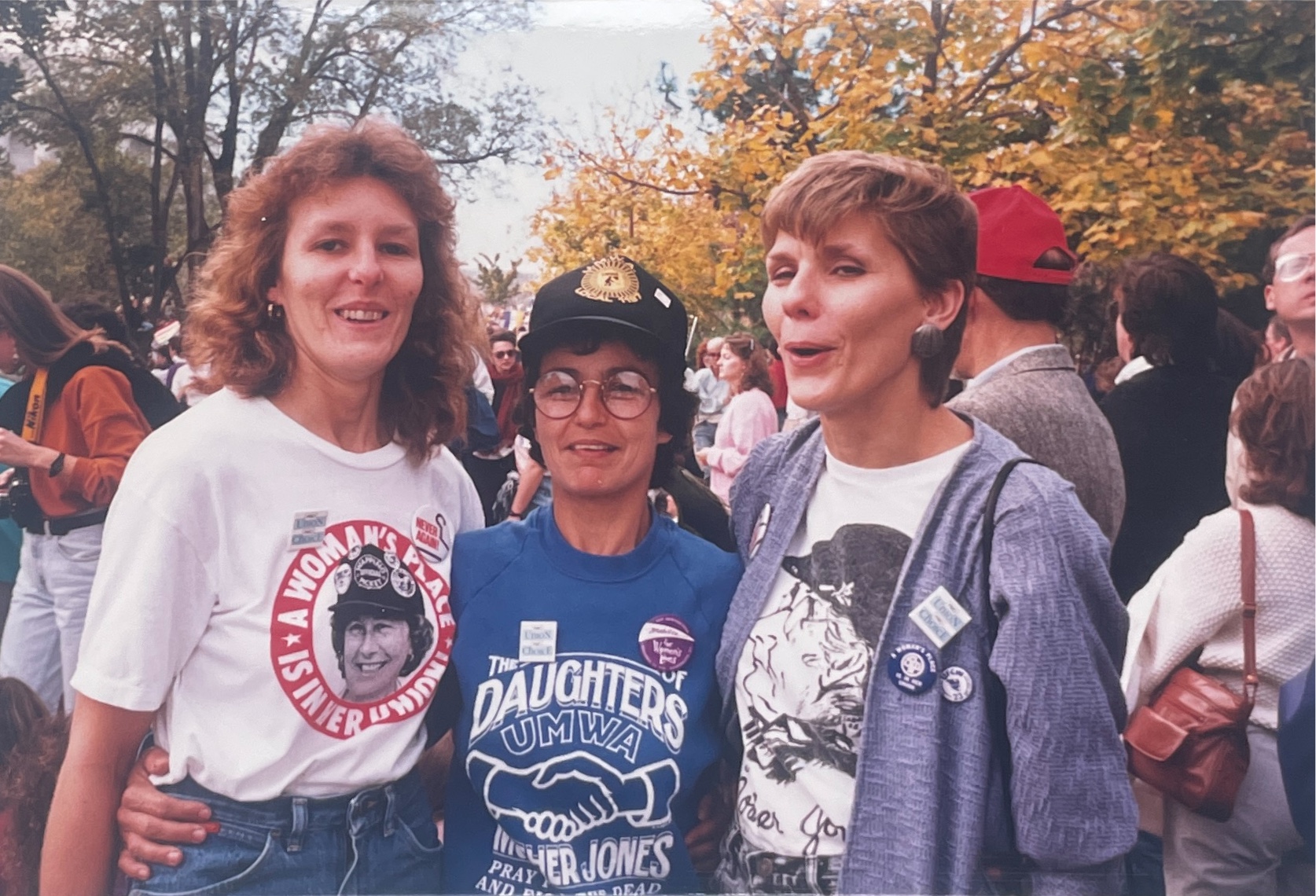 A photo of Kipp Dawson in between two other women, wearing buttons and shirts in support of the Daughters of UMWA.