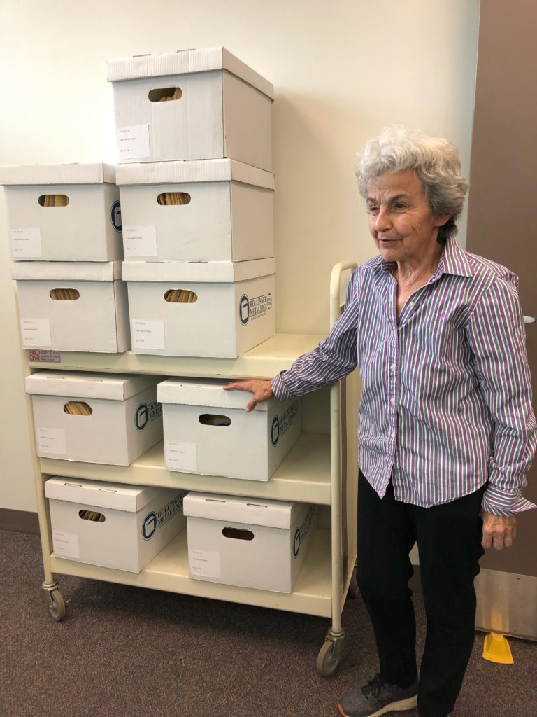 An older Kipp Dawson stands to the right of a stack of 9 file boxes on a rolling cart.